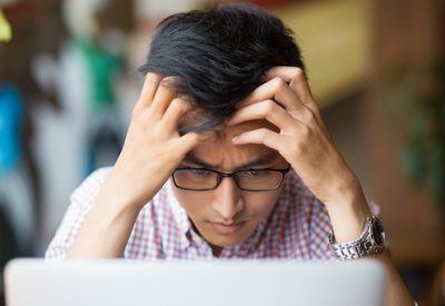 Featured image of a man looking at a laptop with a concerned expression, illustrating the impact of sleep deprivation on mood.